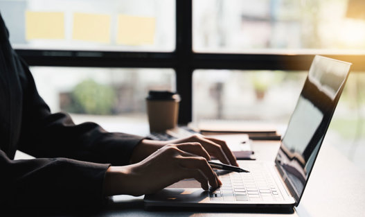 Person från sidan som håller i en penna och knappar på en laptop